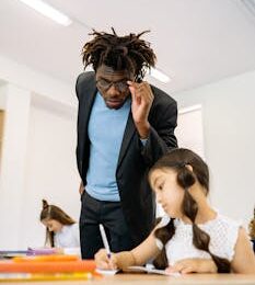 Teacher assisting young student with learning in a bright classroom environment.